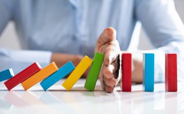 Businesswoman Stopping Dominoes On Desk